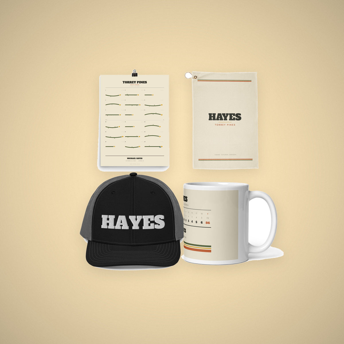 A gift set laid out on cream: course print, golf towel, embroidered hat and scorecard mug